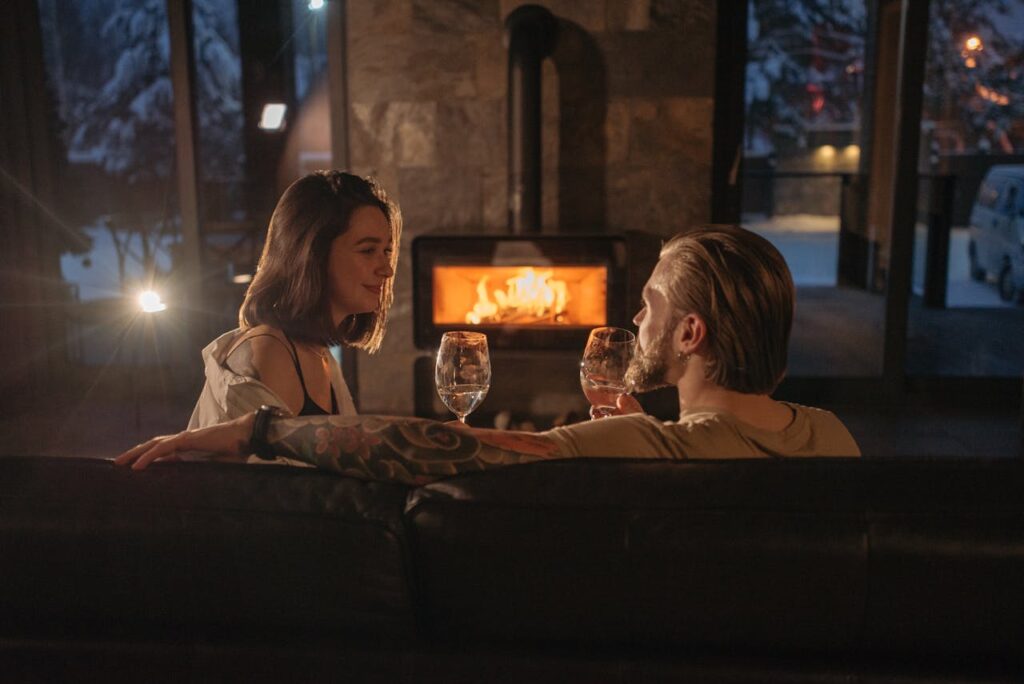 A couple enjoying a cozy, romantic evening indoors by the fireplace with wine glasses.